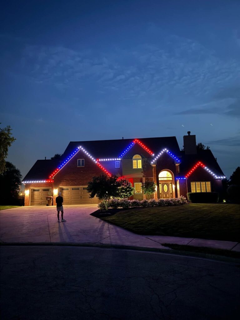 Red, white and blue permanent lights on a two-story home at dusk