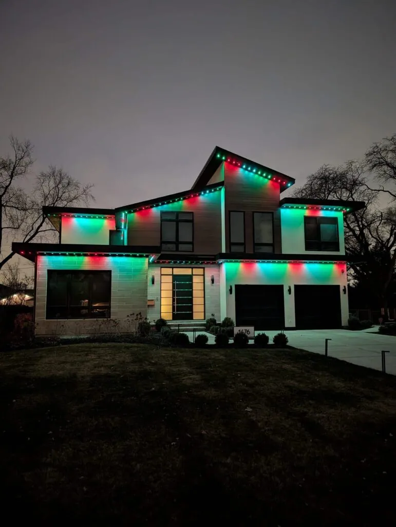 Teal and red permanent lights along a two-story roofline at night