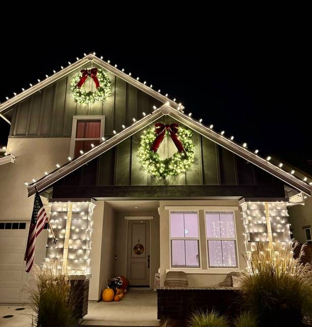 Christmas lights on porch columns, with two lit wreaths on a craftsman-style home