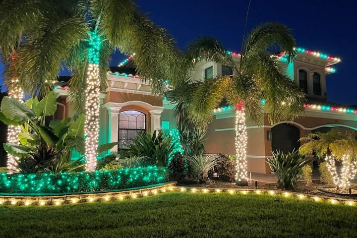 Mediterranean-style home with teal and red Christmas lights on the palm tops