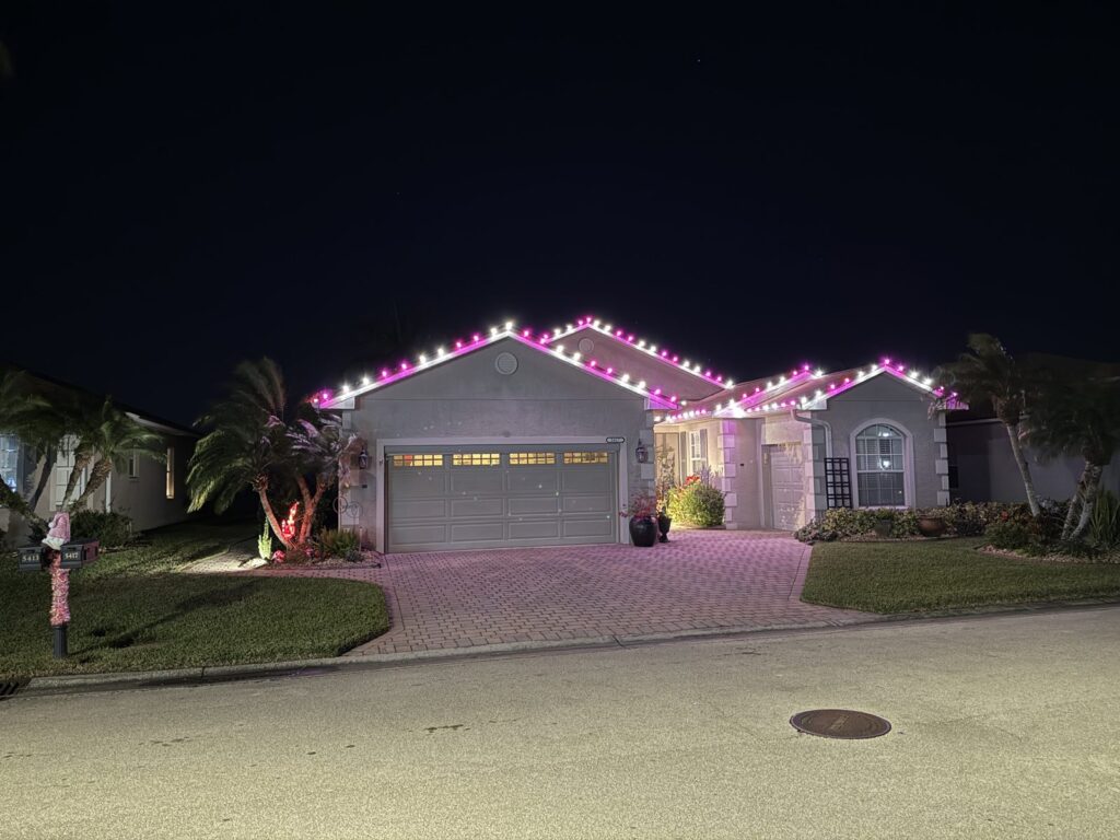 Pink and white Christmas lights along the roofline of a stucco home