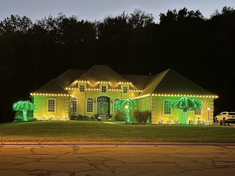 Stucco home with a warm white Christmas light roofline and green-wrapped palm trees